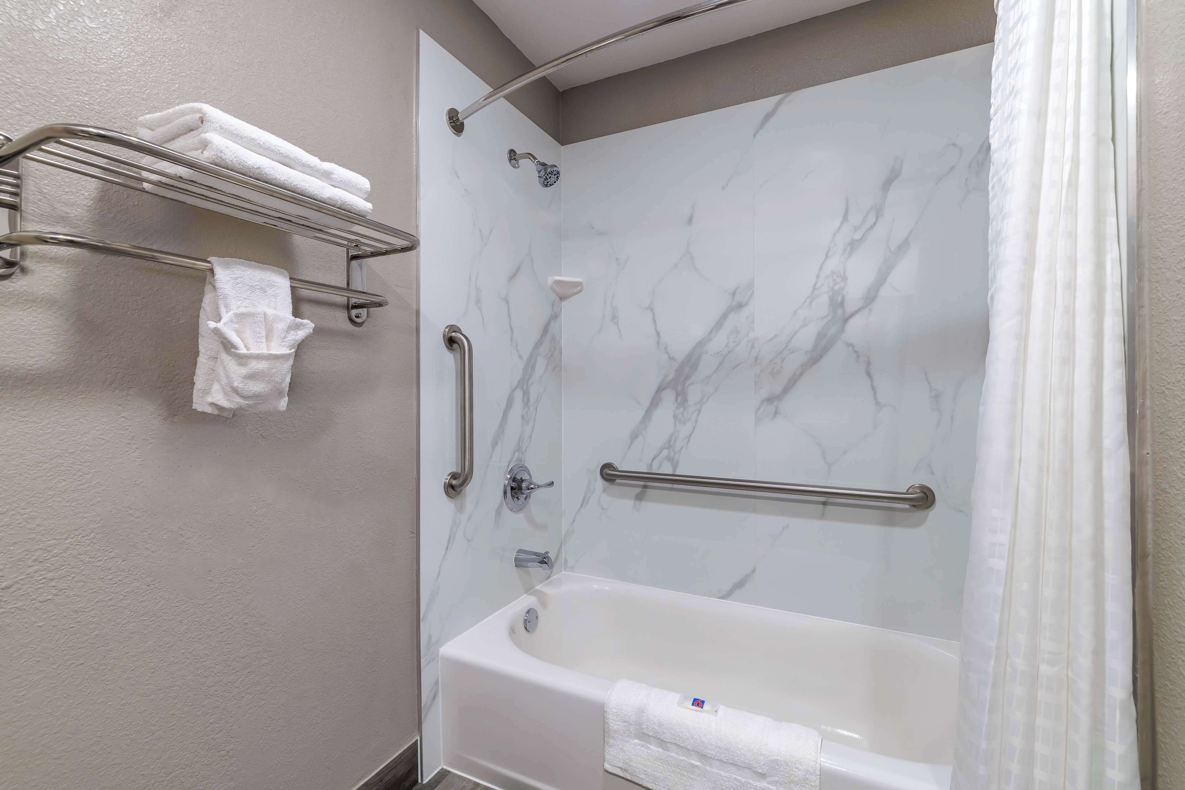 A bathroom with a marble shower wall, a bathtub, and a towel rack with towels.