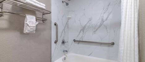 A bathroom with a marble shower wall, a bathtub, and a towel rack with towels.