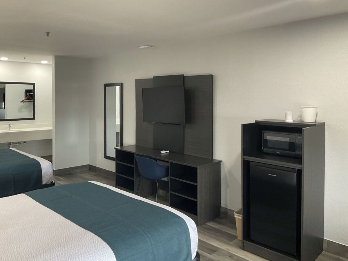Ett hotellrum med två sängar, ett skrivbord med en stol, en platt-TV, en mikrovågsugn och ett litet kylskåp.
