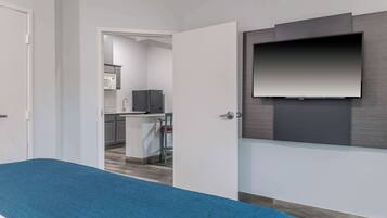 A modern hotel room with a bed, a TV mounted on the wall, and a view into the kitchen area.