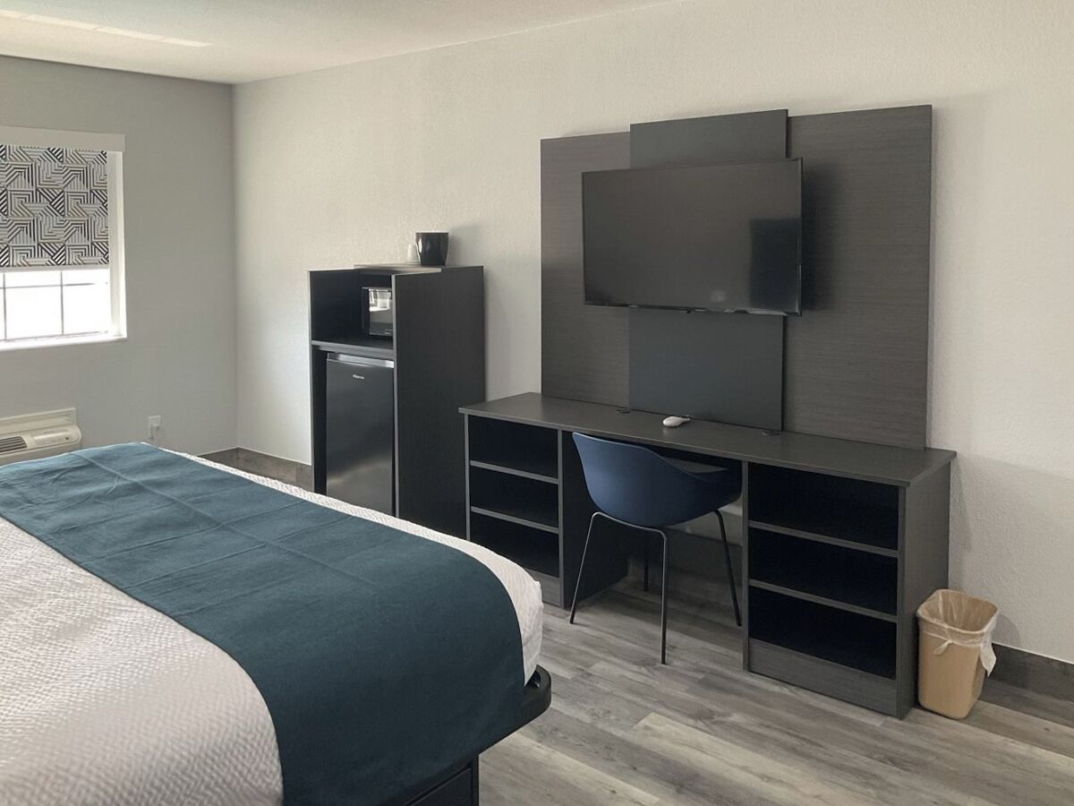 Een moderne hotelkamer met een bed, een bureau, een stoel, een televisie en een kleine kitchenette.