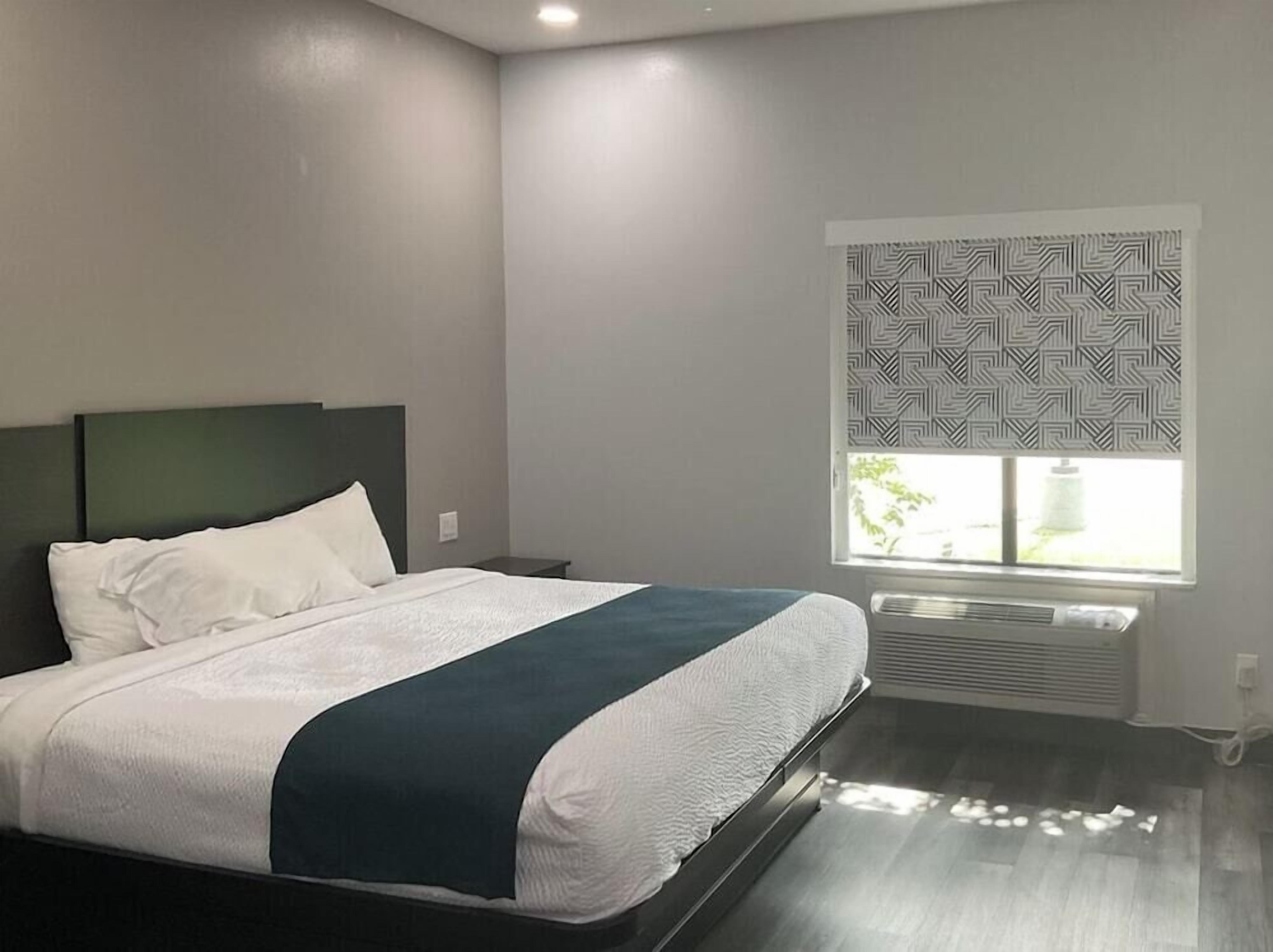 Une chambre d’hôtel moderne avec un grand lit, une table de chevet, une fenêtre avec des stores à motifs et un climatiseur fixé au mur.