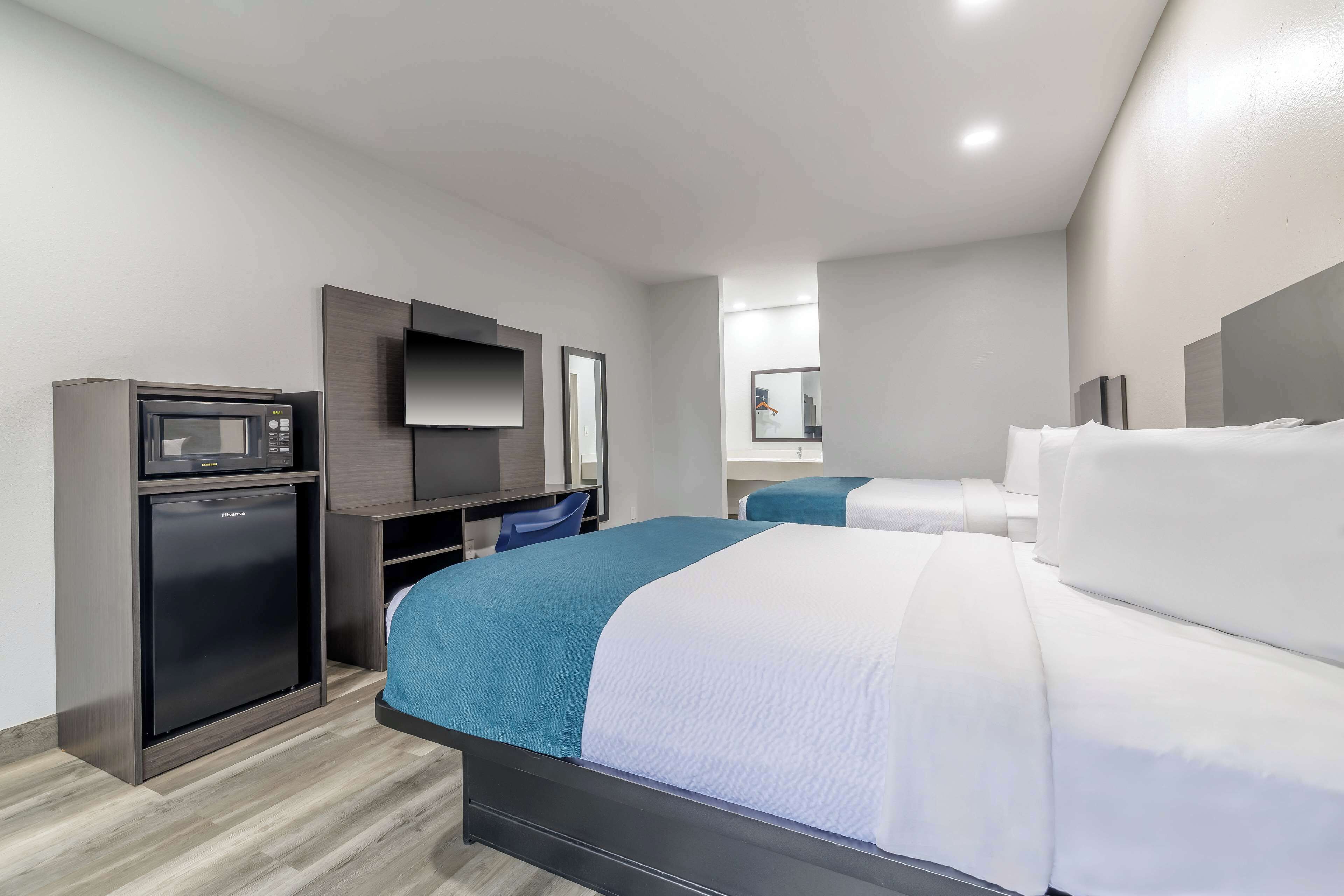 A hotel room with a bed, a small refrigerator, a desk with a chair, and a television.