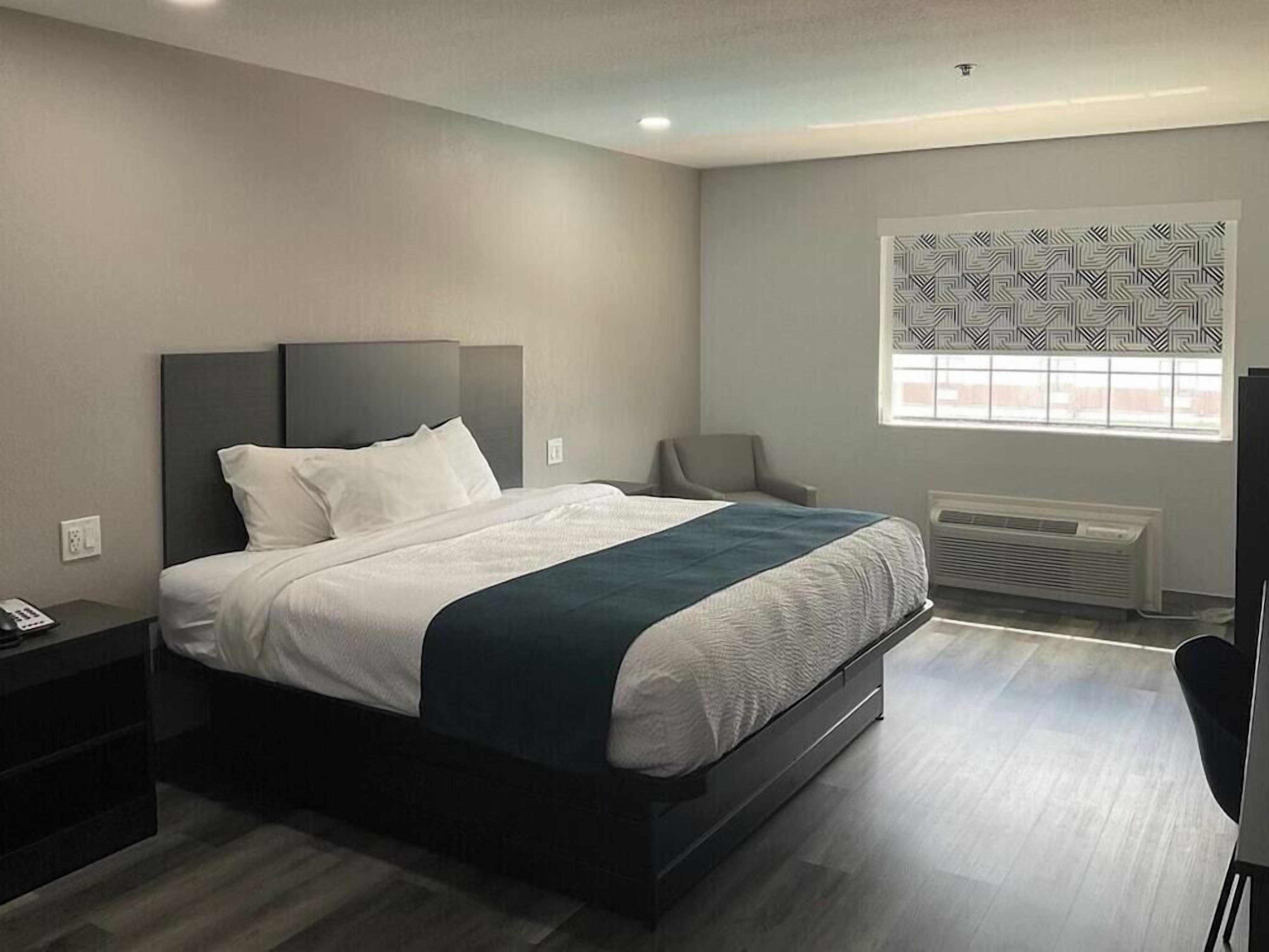 Een moderne slaapkamer met een bed, nachtkastje, stoel en een raam met behang gordijnen.