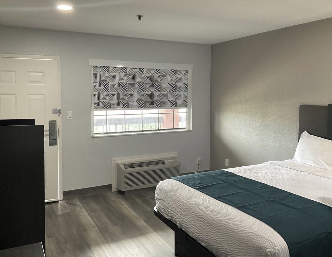 A bedroom with a bed, a window with patterned blinds, a radiator, and a door.