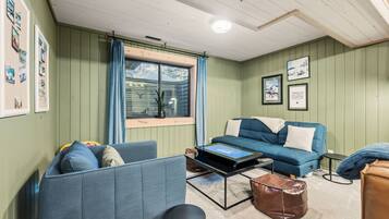 A cozy room with a blue sofa, a coffee table, and a window with curtains.