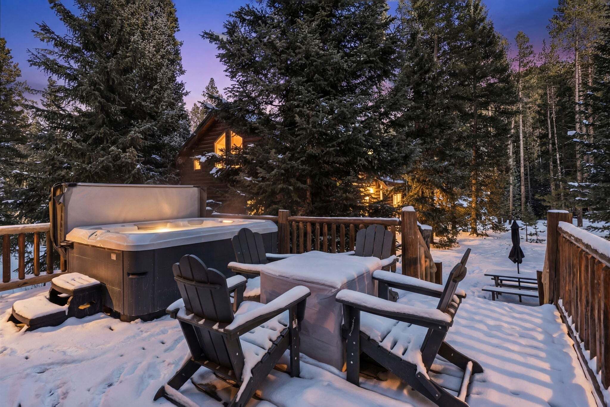 Une terrasse en bois avec un jacuzzi, des sièges d’extérieur et un chalet en arrière-plan.