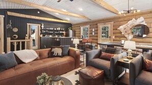Ein Holzblockhaus-Interieur mit einem gemütlichen Wohnbereich, der Ledersofas, einen Couchtisch und einen Kamin umfasst.