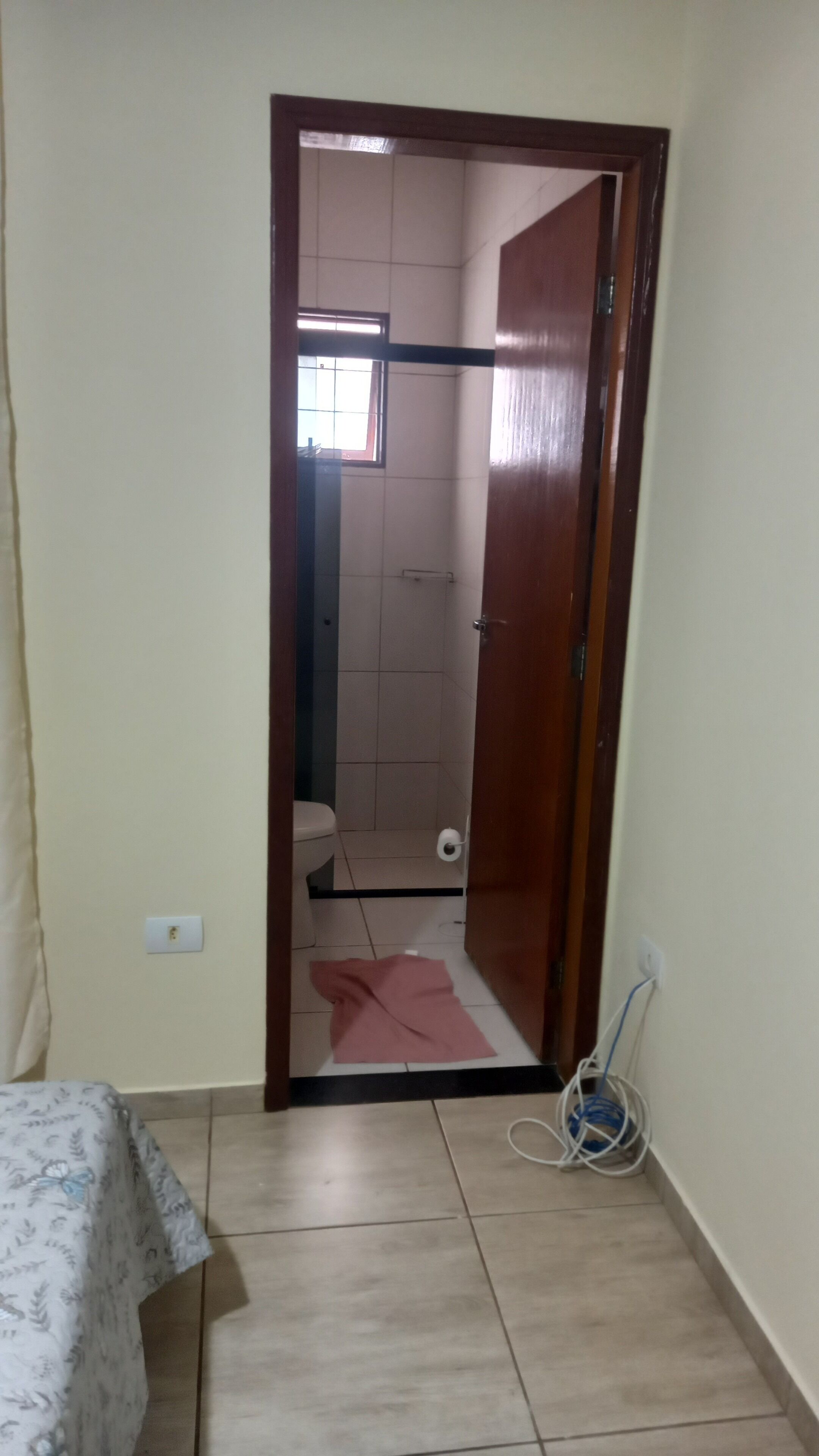 Een smalle gang die uitkomt bij een badkamer met een toilet, een douche en een raam.