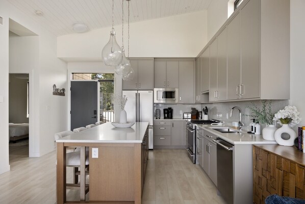 A modern kitchen with a central island, stainless steel appliances, and light wood cabinetry.