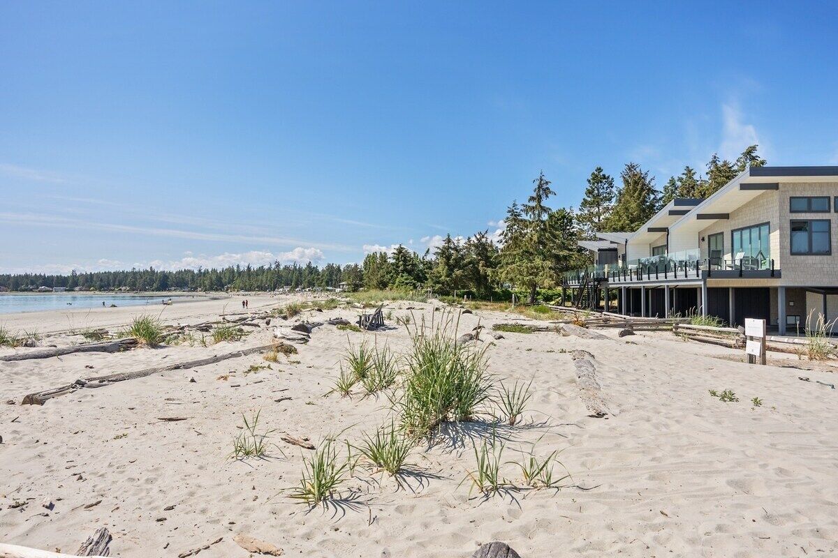 Une propriété située en bord de mer, dotée d’une architecture moderne, comprenant un grand bâtiment avec de nombreux balcons et une structure plus petite à proximité.