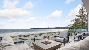 A beachside patio with a fire pit, outdoor seating, and a view of the ocean. - Beachfront Luxury Suite #19 at THE BEACH HOUSE (Campbell River)