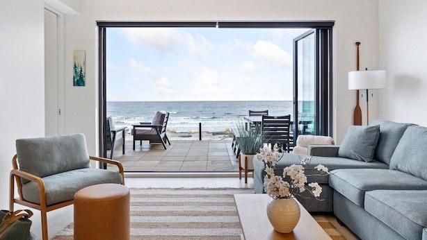 A modern living room with a view of the ocean, a sofa, a chair, and a dining area with outdoor seating. - Beachfront Luxury Suite #19 at THE BEACH HOUSE (Campbell River)