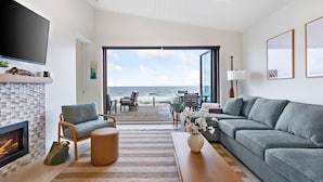 A modern living room with a fireplace, a sofa, a TV, and a view of the ocean. - Beachfront Luxury Suite #19 at THE BEACH HOUSE (Campbell River)