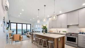A modern kitchen with a large island, stainless steel appliances, and a view of the ocean. - Beachfront Luxury Suite #19 at THE BEACH HOUSE (Campbell River)