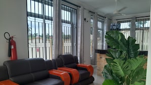 Un salon moderne avec un canapé en cuir noir, une grande plante en pot et un balcon offrant une belle vue.