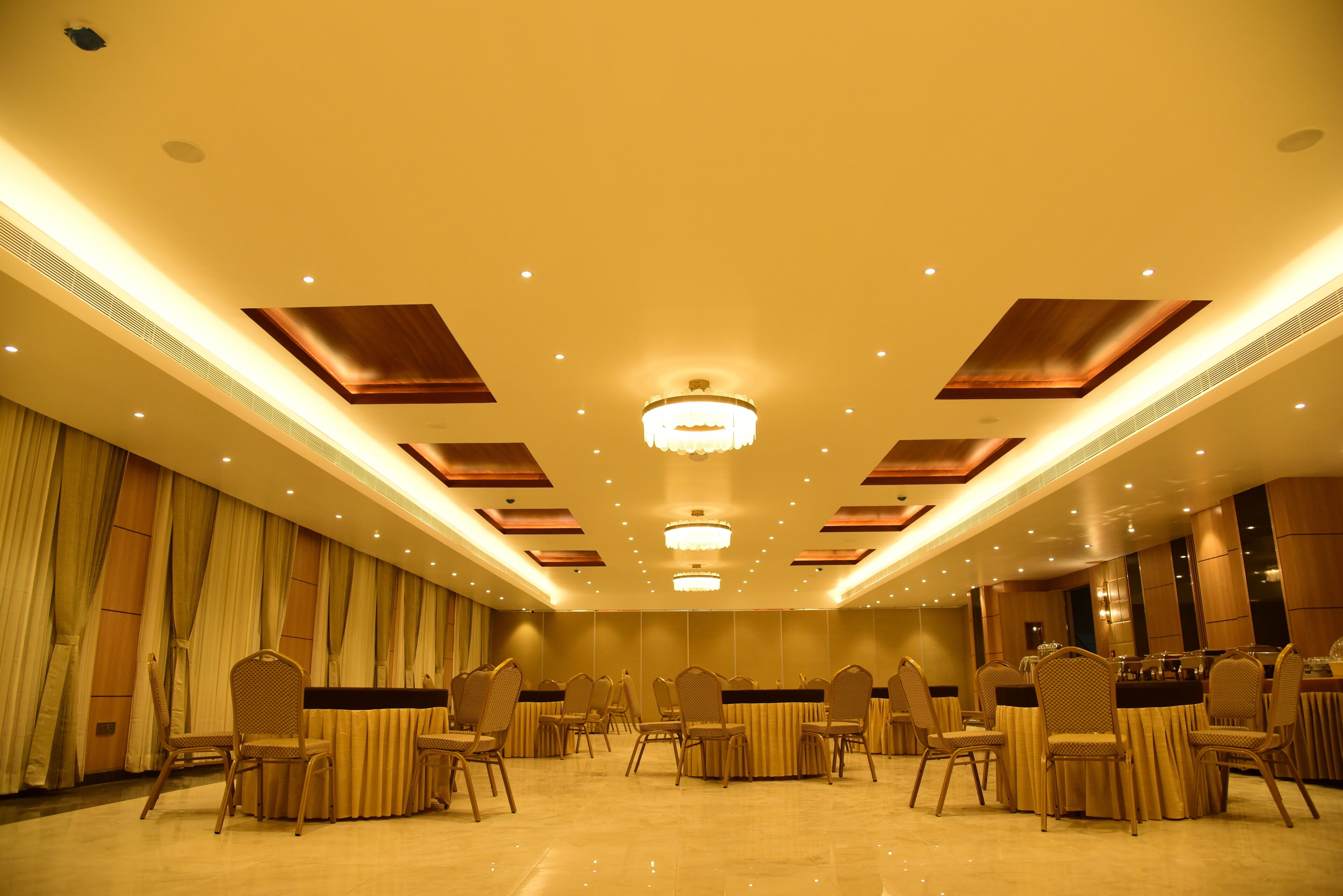 A spacious banquet hall with high ceilings, recessed lighting, and a central chandelier.