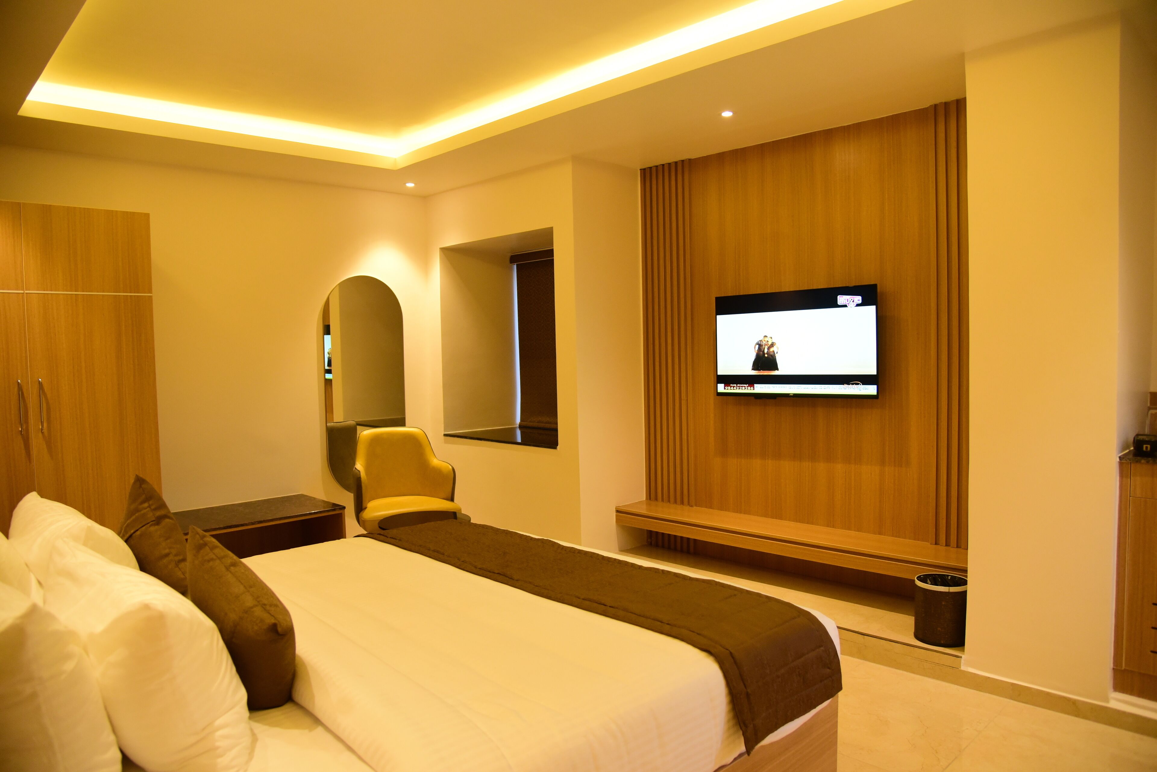 Una habitación de hotel moderna con una cama grande, un televisor montado en la pared y un armario de madera.