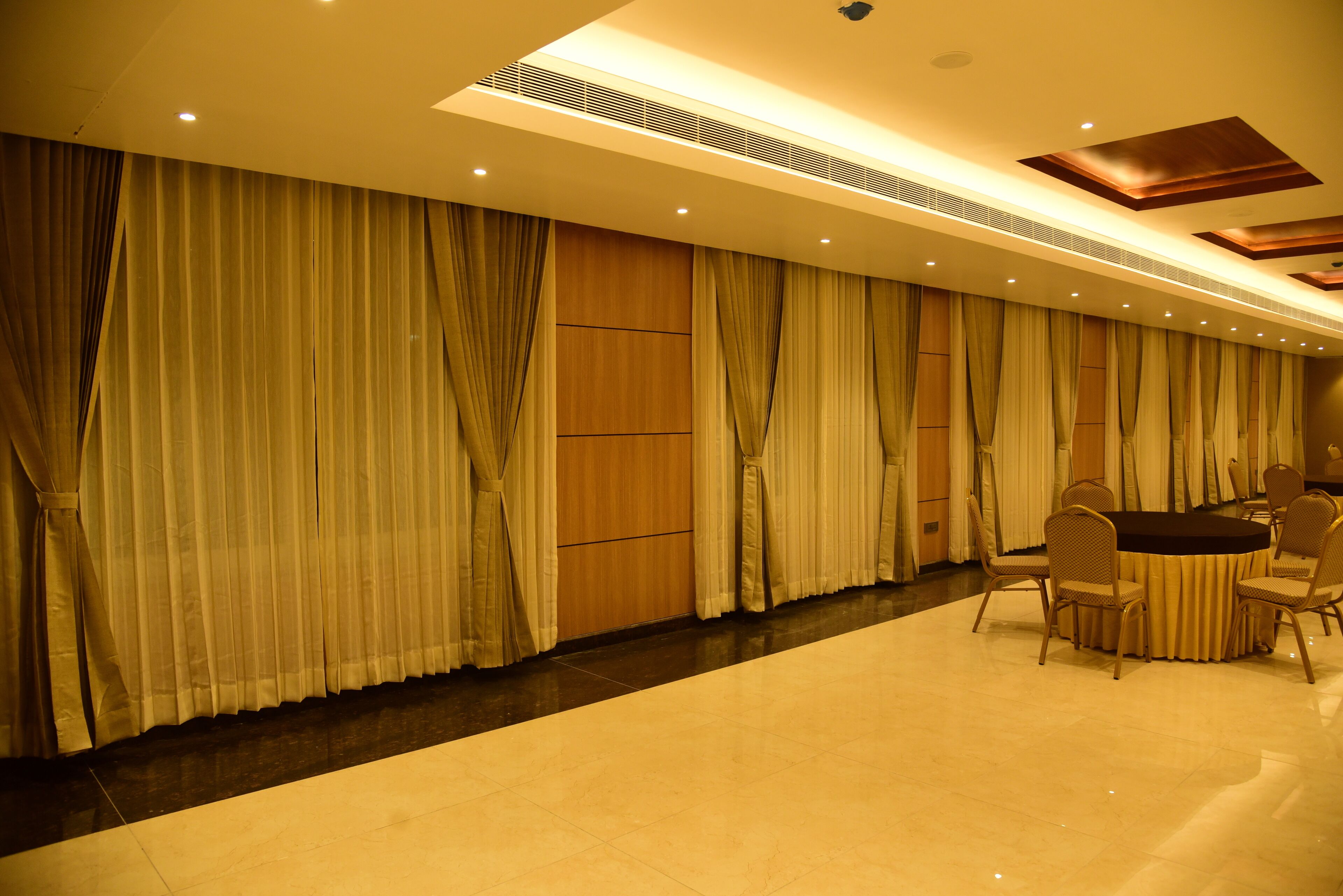 A conference room with a round table and chairs, large curtains, and recessed lighting.