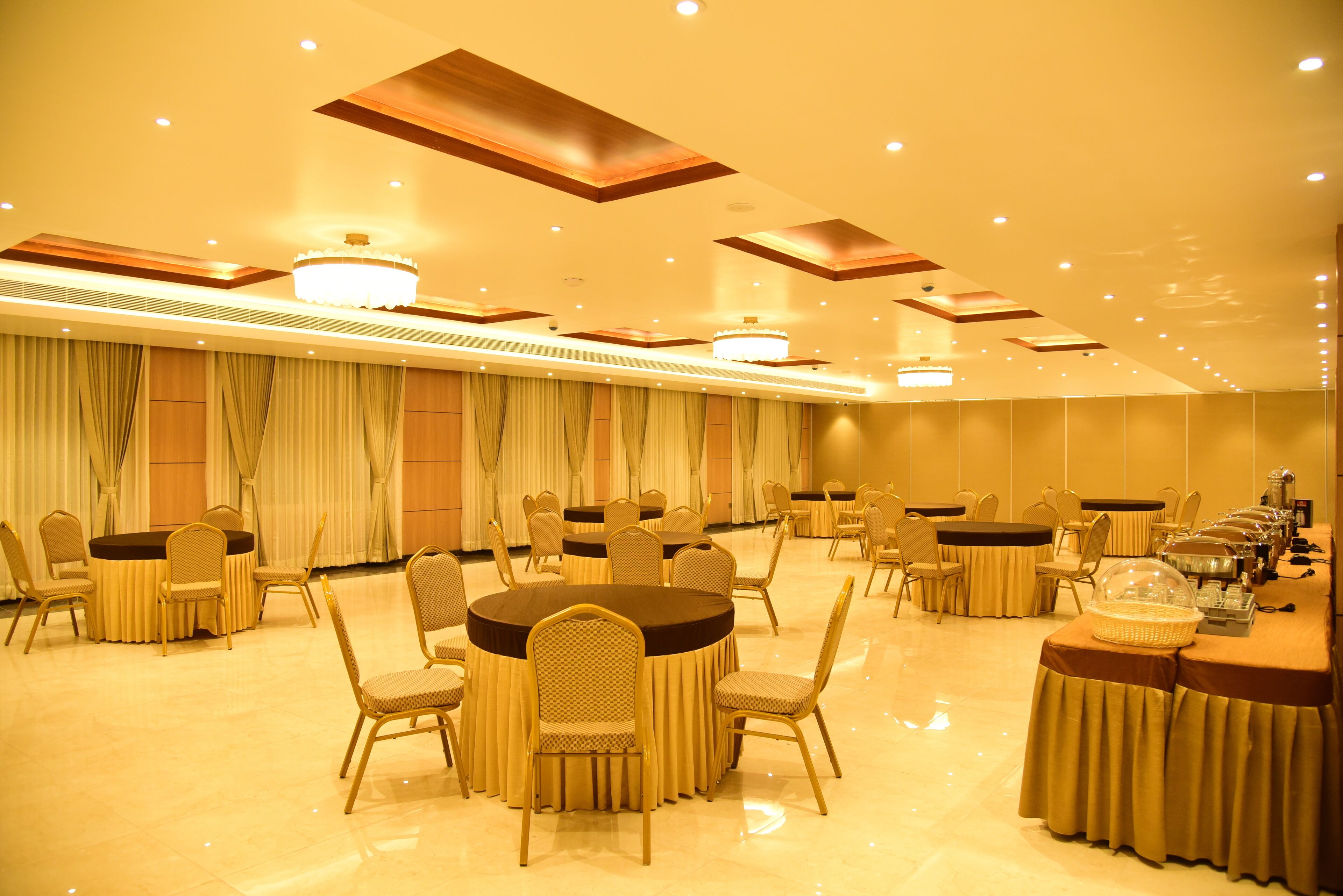 Une salle de banquet avec des tables rondes et des chaises, un éclairage encastré et un lustre.