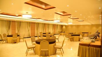 Un salón de banquetes con mesas y sillas redondas, iluminación empotrada y una araña.