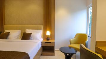 Habitación de hotel con una cama grande, una mesita de noche con lámpara, una pequeña mesa redonda y un sillón amarillo.