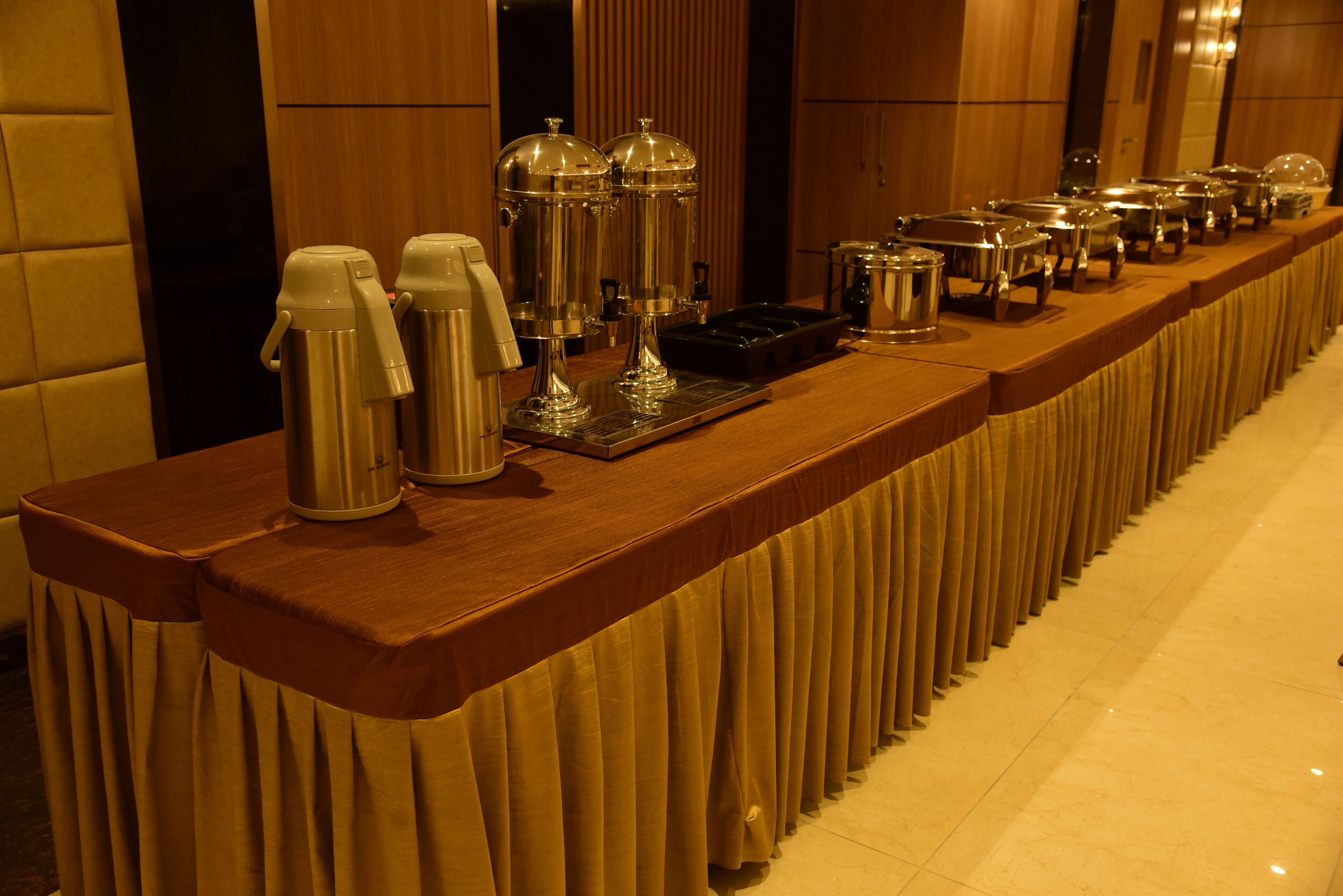 A buffet setup with various food and drink dispensers on a long wooden table.