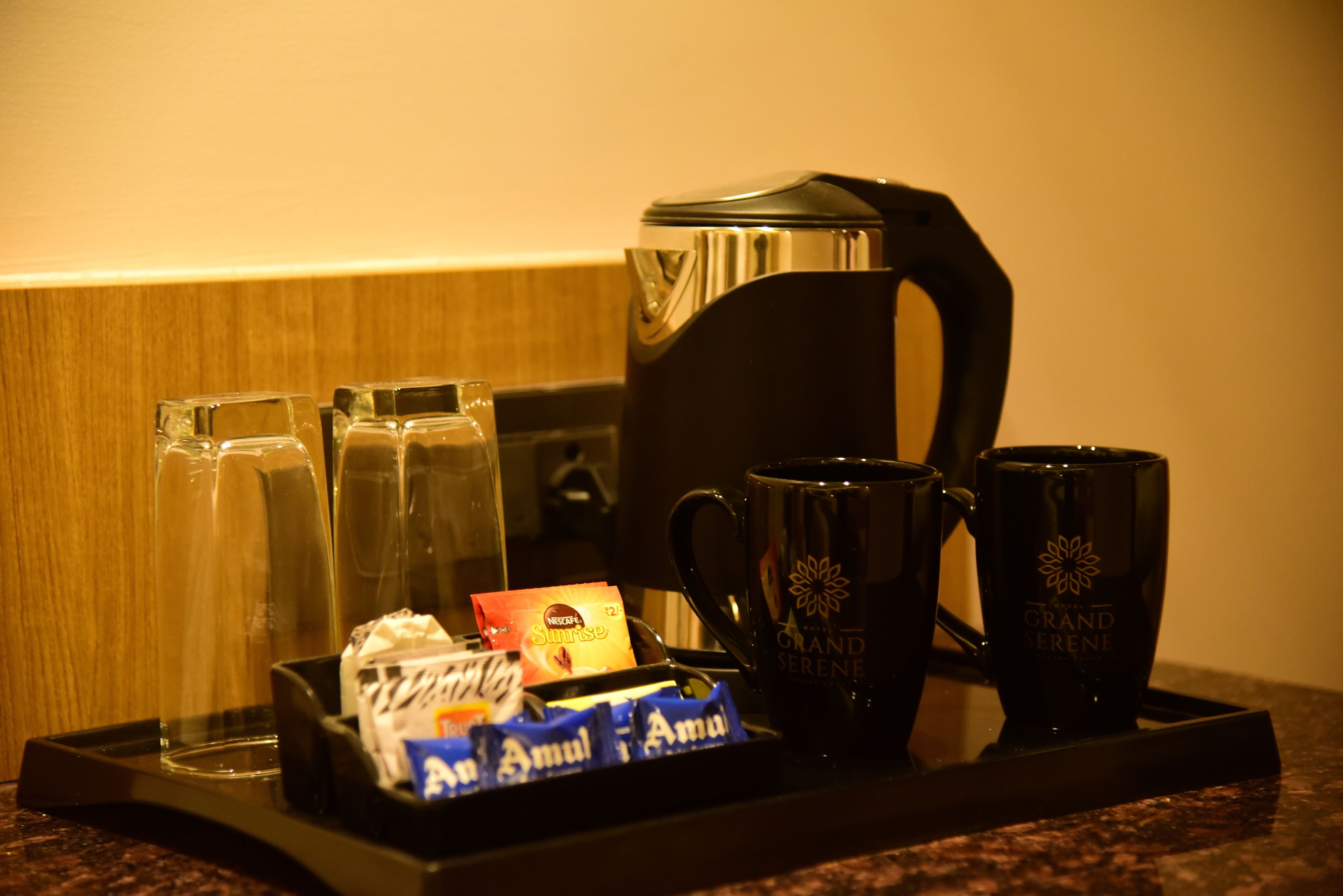 A tray with a coffee maker, two glasses, two mugs, and some packaged snacks.