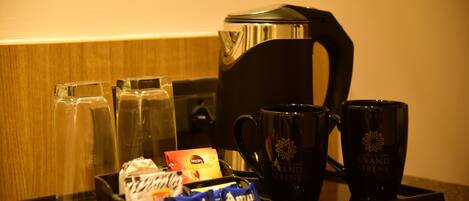 A tray with a coffee maker, two glasses, two mugs, and some packaged snacks.