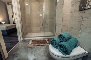 Een moderne badkamer met een douche met glazen wand, een wit toilet en een blauwgroene handdoek op het toilet.
