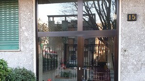 L'ingresso di un edificio con una porta in vetro, un piccolo giardino fiorito e un vialetto in pietra che conduce alla porta.