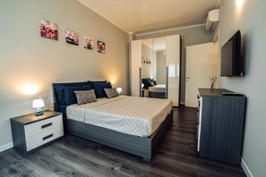 Een moderne slaapkamer met een bed, nachtkastjes, een dressoir en een flatscreen televisie.