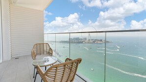 Un balcon agrémenté de fauteuils en osier et d’une table en verre, offrant une vue sur un port de plaisance avec des bateaux et une grande roue.