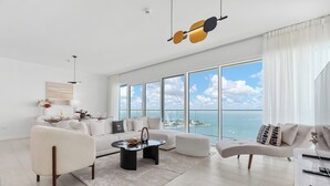 Un salon spacieux doté d’une grande fenêtre donnant sur la mer, d’un lustre moderne et d’un aménagement minimaliste.