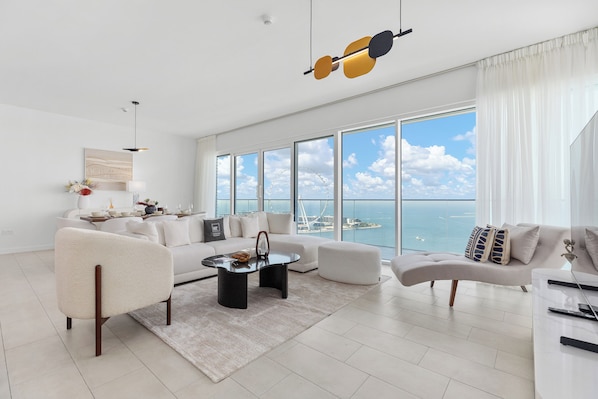 A spacious living room with a large window overlooking the sea, a modern chandelier, and a minimalist design.