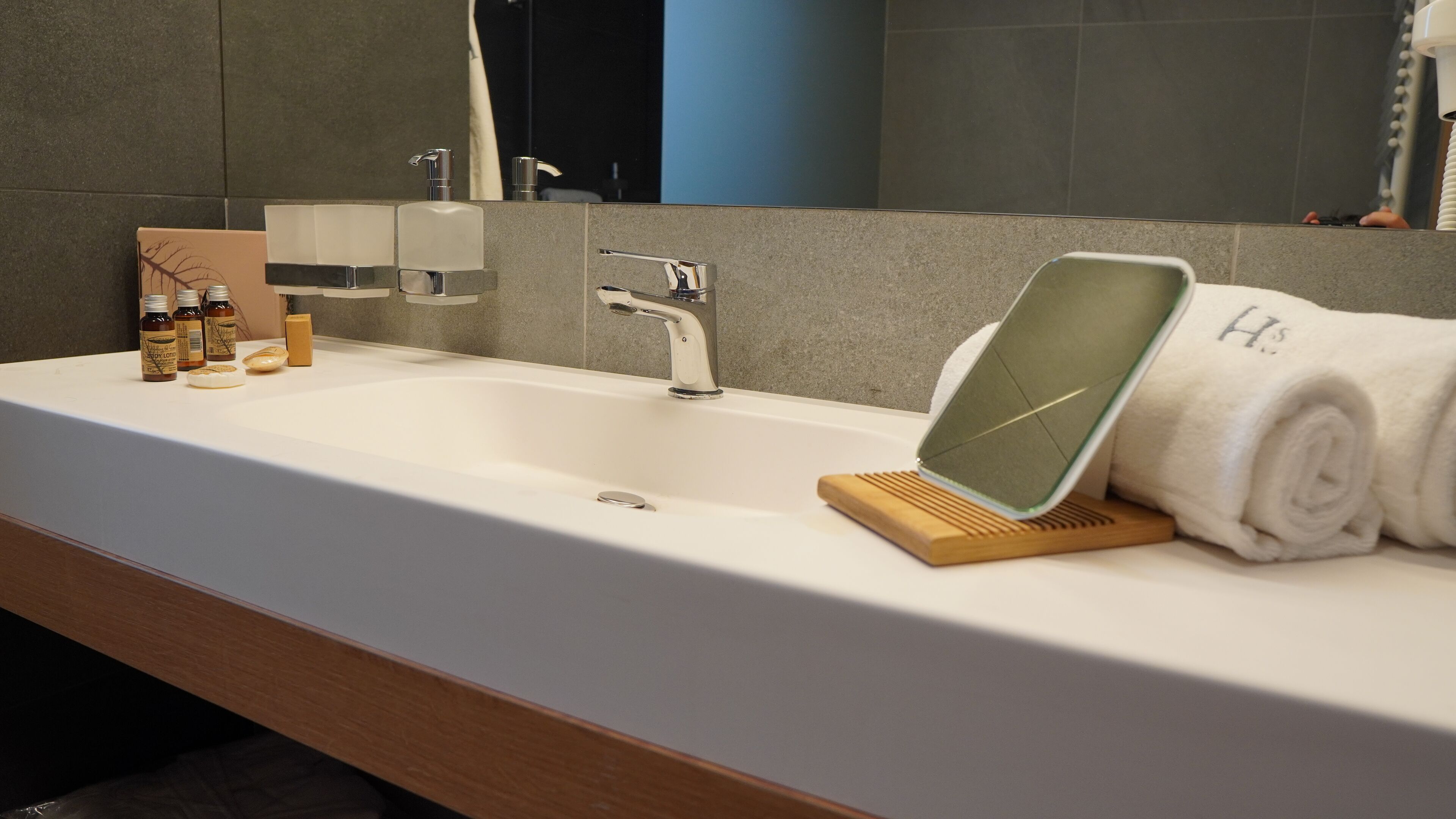 A modern bathroom with a white sink, a mirror, and toiletries.