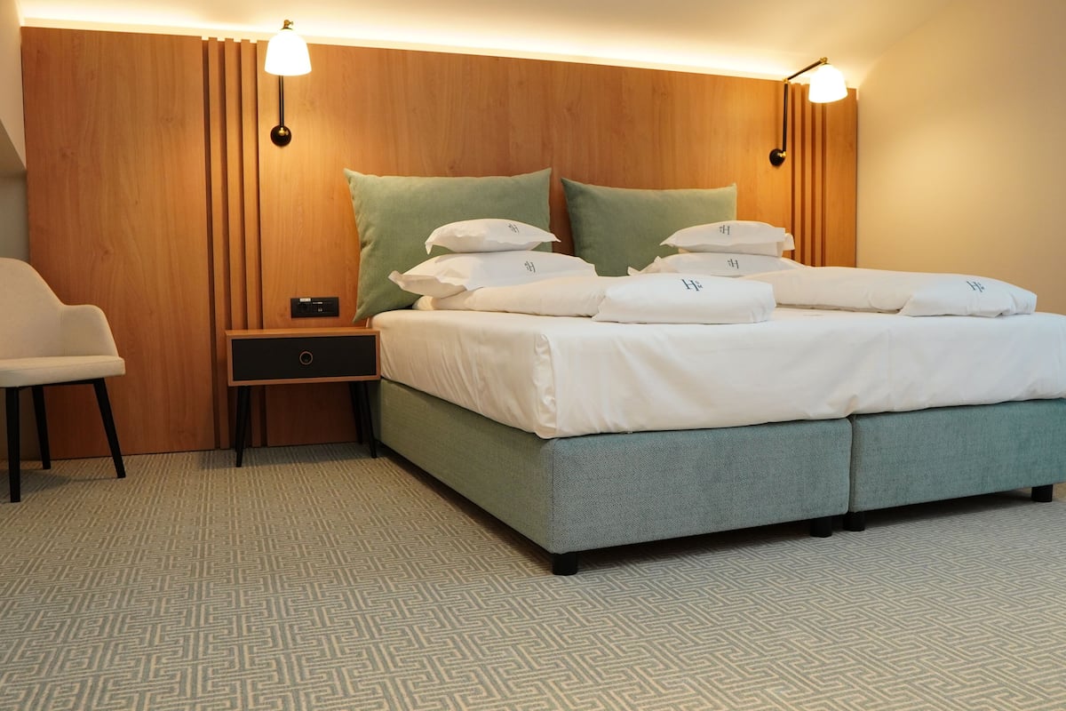 A hotel room with a bed, nightstand, chair, and wooden headboard.