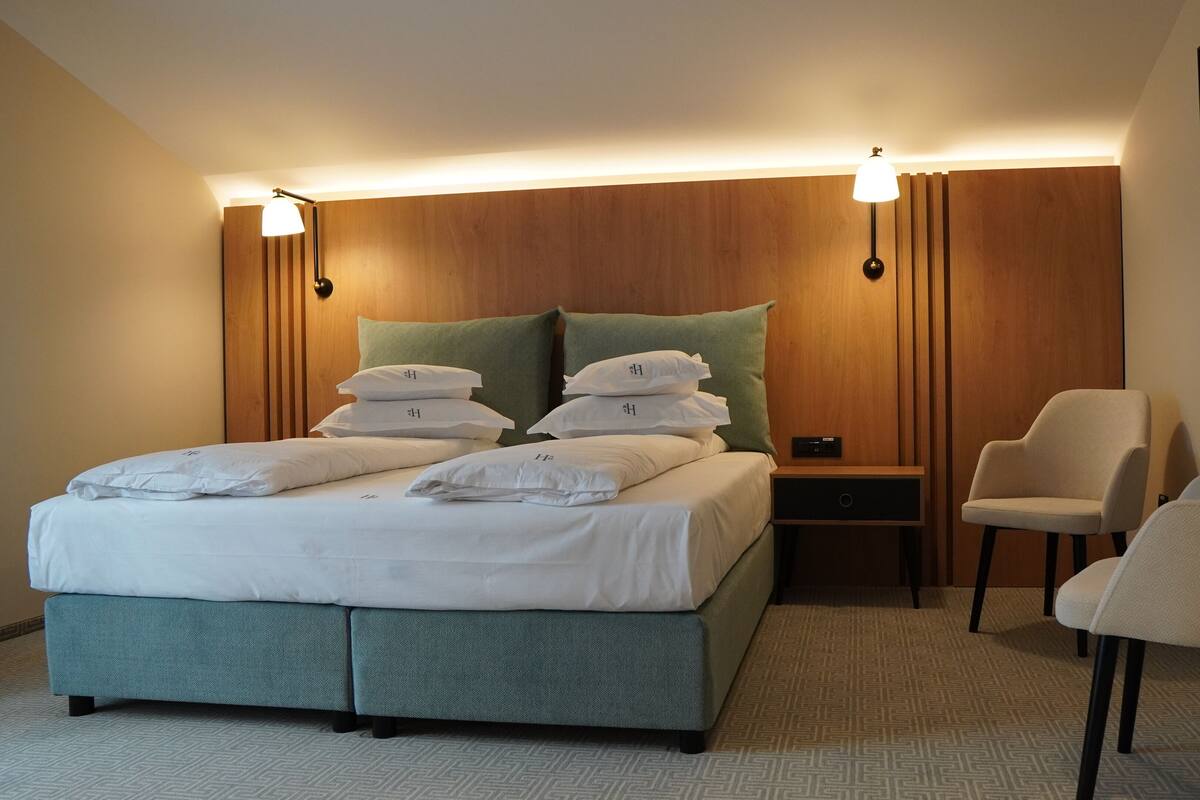 A neatly arranged hotel room with a bed, bedside tables, a chair, and a wall-mounted artwork.