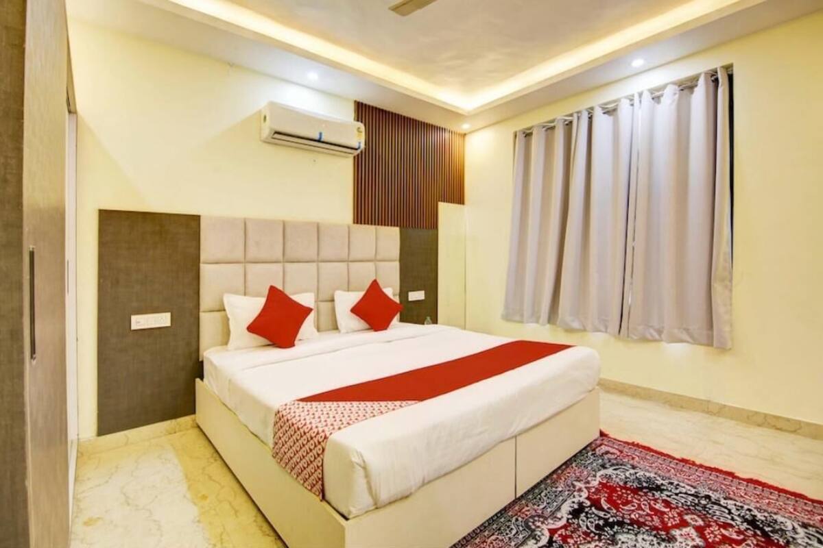 Ein Schlafzimmer mit einem Bett, einer roten und weißen Tagesdecke, einem gemusterten Teppich und einem Fenster mit Vorhängen.