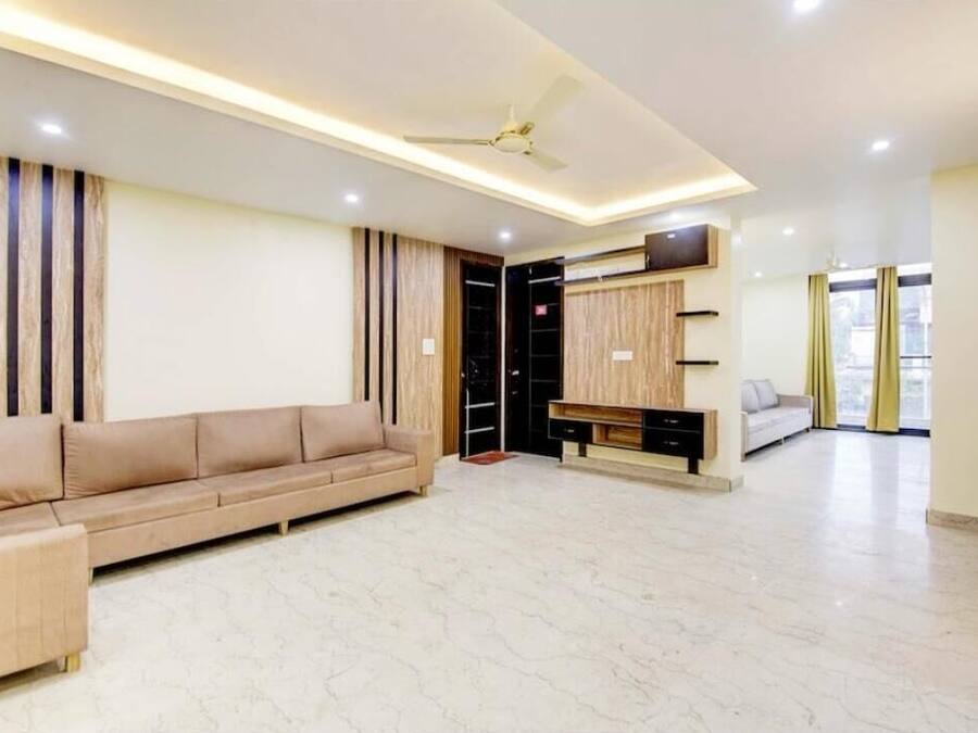 Uma sala de estar espaçosa com um sofá bege, um ventilador de teto e um painel para a TV.