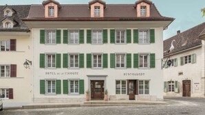 Un bâtiment à deux étages avec des volets verts, portant les inscriptions « HÔTEL DE LA CIGOGNE » et « RESTAURANT » au rez-de-chaussée.