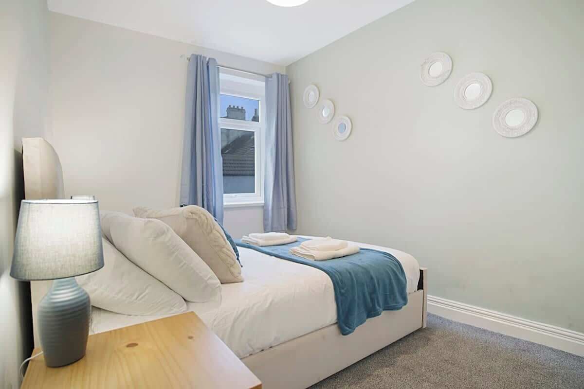 A bedroom with a bed, a nightstand, a lamp, a window with curtains, and wall decorations.