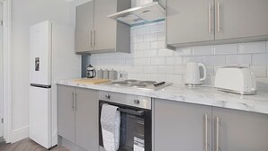 A modern kitchen with grey cabinets, a white refrigerator, a stove, and a coffee maker. - Seaside Haven on Newcomen Grove, Redcar Retreat (Redcar and Cleveland)