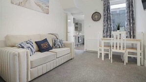 A living room with a sofa, a dining table with chairs, a clock, and a window with curtains. - Seaside Haven on Newcomen Grove, Redcar Retreat (Redcar and Cleveland)