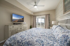 Habitación de hotel con cama, televisión, ventilador de techo y vista a la ciudad por la ventana.
