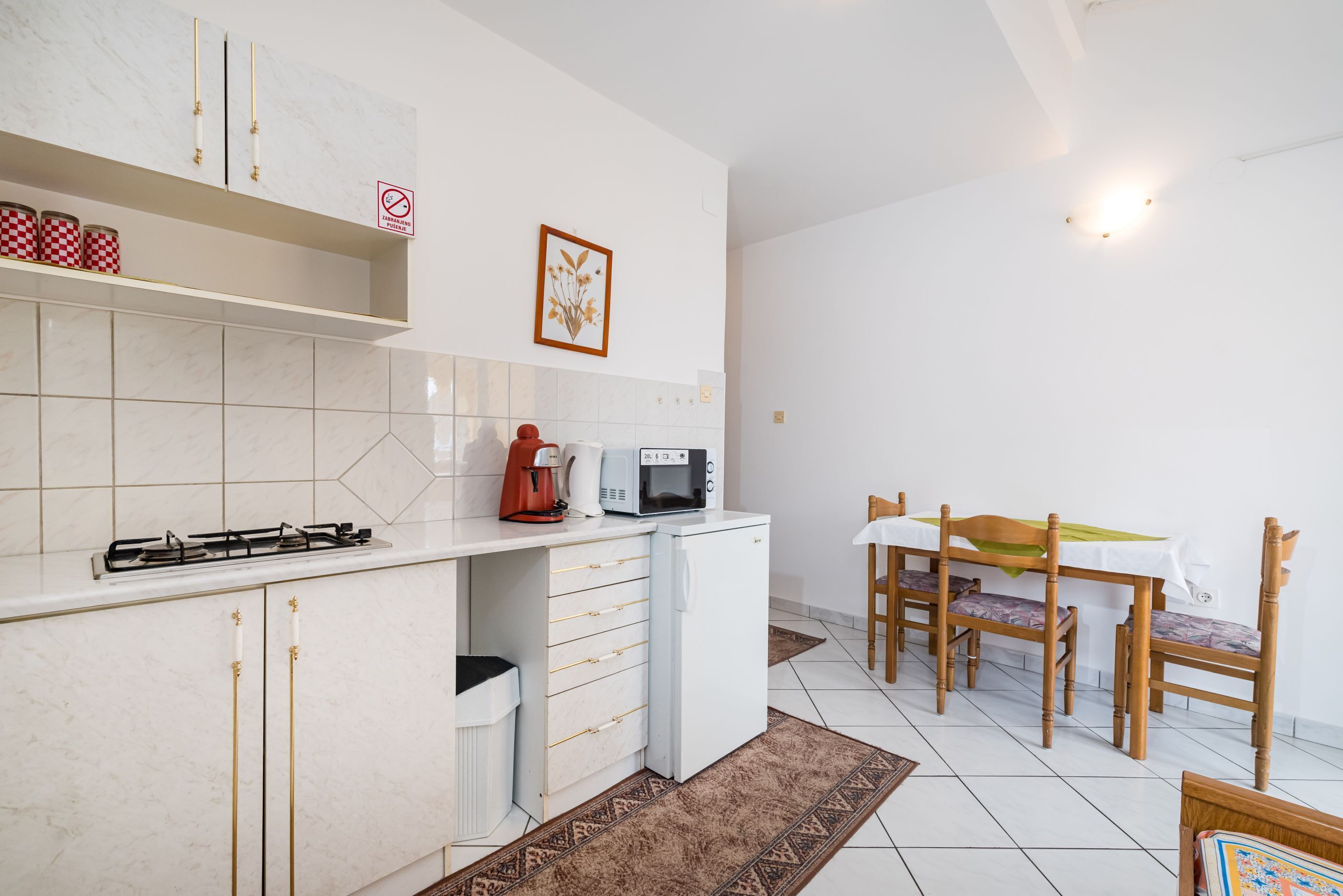 A compact kitchen with a gas stove, microwave, and a small refrigerator. There is a dining area with a table and chairs, and a patterned rug on the floor.