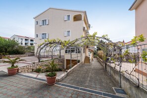 Un edificio residencial con un corredor cubierto, plantas en macetas y una valla de metal.