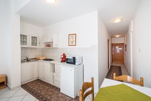 Una cocina compacta con armarios blancos, un microondas, un refrigerador pequeño y una zona de comedor con mesa y sillas.