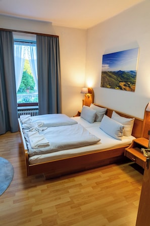 Un lit double avec du linge de lit blanc, une table de chevet avec une lampe, un tableau au mur et une fenêtre avec des rideaux.