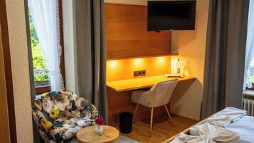 A hotel room with a bed, a desk with a chair, a TV mounted on the wall, and a window with curtains.